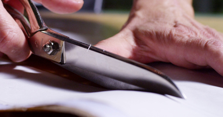 A dressmaker cutting a high quality white fabric, before you sew it and make a piece of high...