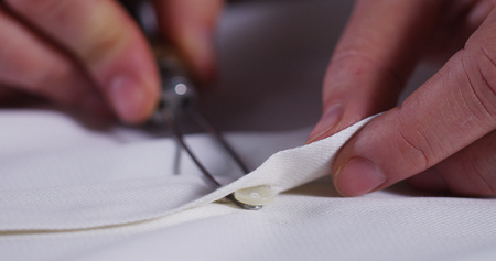 A hand of a young seamstress wearing a white cloth tailoring to the tradition of tailors. The...