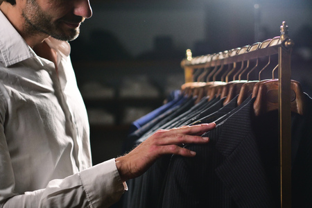 A handsome man with a white shirt, is choosing a jacket from the clothes hangersの写真素材