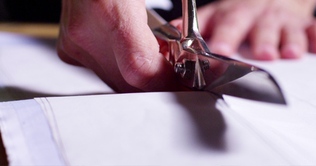A dressmaker cutting a high quality white fabric, before you sew it and make a piece of high...