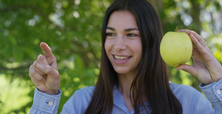 Beautiful young girl holding a fresh ripe apple in the hands, in the background of nature. Concepts:...