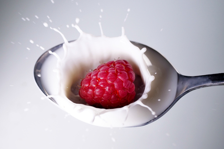 Close up of a raspberry falling down in a spoon full of milk. Concept: Breakfast, diet, summer
