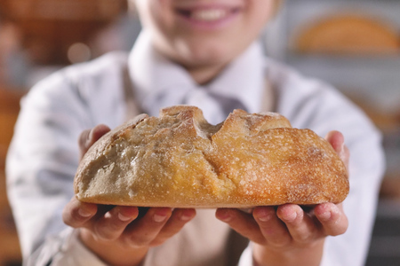 Close up of a baker little helper showing the bread just pulled out of the oven. Concept of: artisan, baker, raw materials, love for food and traditionsの写真素材