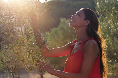 Beautiful girl in a red dress is enjoying the nature in a garden among the olive treesの写真素材