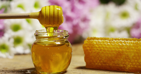 biological and genuine honey drips inside a jar. honeycomb dripping honey. black background and a wooden table.の写真素材