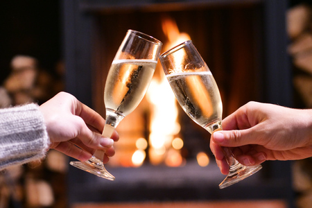 One winter couple sitting in front of a fireplace relaxing, drinking a glass of champagne and making a toast while enjoying the warmth of the fireplace.の写真素材