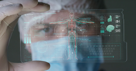 A futuristic physician, a surgeon, examines a technological digital holographic plate, a medical mask, a cap, brown eyes. Concept: futuristic medicine, new technologies, doctors, laboratory, future.の写真素材