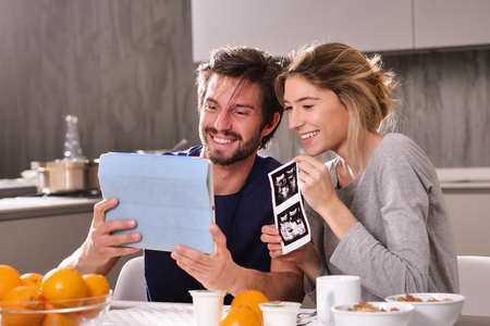 A couple in love videocall their parents using a tablet, to announce the birth of their son showing the ultrasound. Concept of: family, birth, life, loveの写真素材