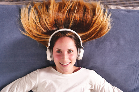 A woman lying on the bed listens to music with wireless headphones and relaxes. The woman dances and dreams with music. Concept of: music, relaxation, dream,の写真素材