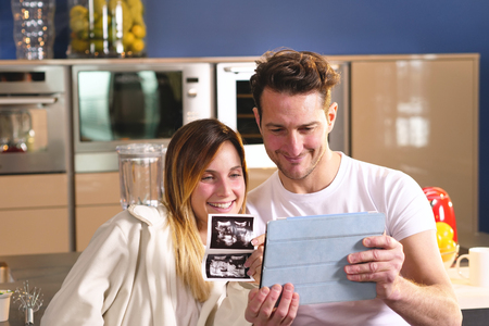 A couple in love videocall their parents using a tablet, to announce the birth of their son showing the ultrasound. Concept of: family, birth, life, loveの写真素材