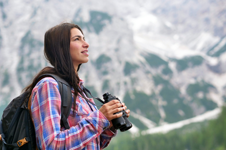 A beautiful woman camping, explore the nature around her with binoculars, look for animals or paths to go. Concept of: curiosity, research, exploration, trekkingの写真素材