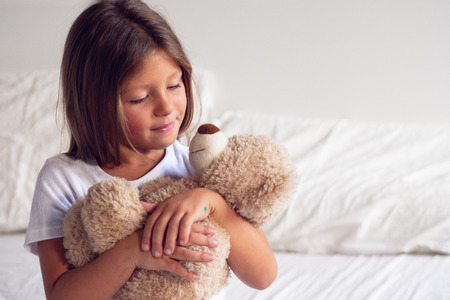 A little girl, wakes up in the morning, smiles, hugs her teddy bear and is happy about how she slept in her bed. Concept of: relaxation, love sleep and wake up in the morningの写真素材
