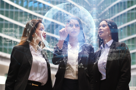 Three business women of different ethnicities, dressed in business suits, and talking about finance and economics looking at futuristic charts with holography. Concept of: female career, technologyの写真素材
