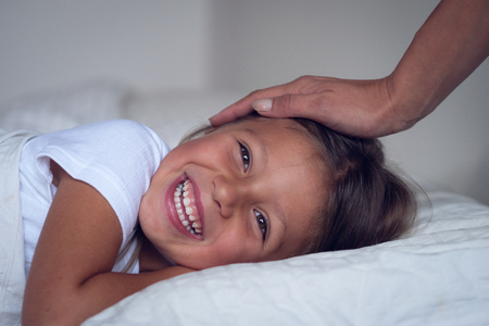A little girl in bed under the white blankets while her mother is stroking her. Concept of: relaxation, family, waking up in the morning and happiness.の写真素材