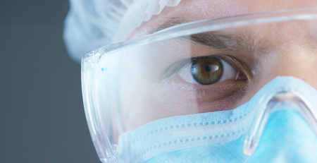 A doctor or surgeon in a medical mask, a respirator, brown eyes, goggles, a surgical cap, a hospital or clinic.