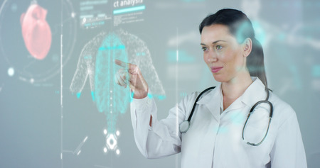 Female doctor with white coat and stethoscope, with holographic tablet representing the patient's body, the heart lungs, muscles, bones.の写真素材