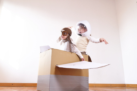 Two sisters in the bedroom dressed as an aviator and astronaut, pretends to drive a paper airplane and imaginesの写真素材