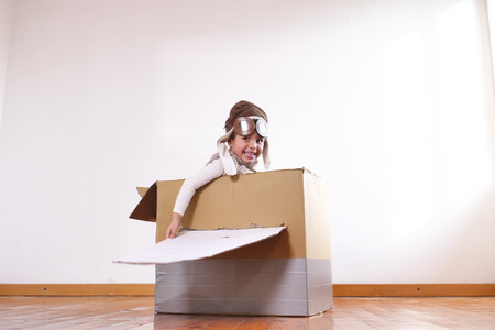 A girl in a bedroom dressed as an airman or a pilot pretends to drive a paper airplane. Concept of: freedom, success, dreams and play.の写真素材