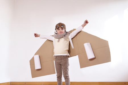 A girl in a bedroom dressed as an airman or a pilot pretends to drive a paper airplane. Concept of: freedom, success, dreams and play.の写真素材
