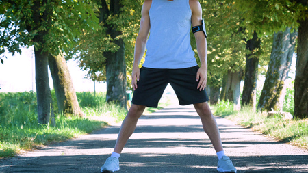 Handsome young guy doing sportsman warm-up, phone holder, smiling, wearing sports clothes, running...