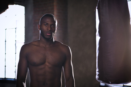 An African American guy trains in a vintage gym and fists his boxing bag fists. Concept of: gym,...