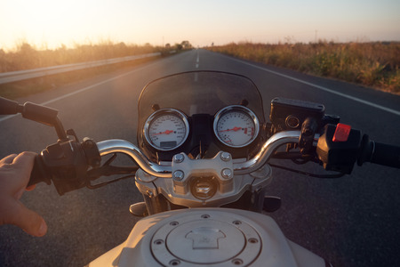 POV of a motorcyclist driving on a road at sunset, his futuristic motorcycle on which the holographic graphics appear. Concept of: travel, transport, road, freedom and relaxation.の写真素材