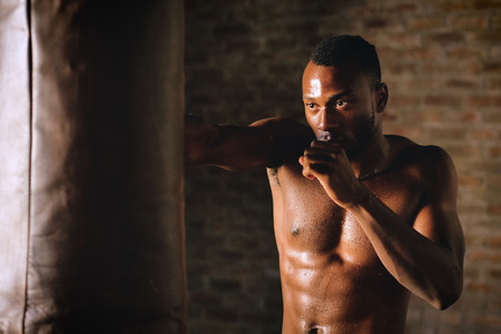 An Afro-american guy trains in a vintage gym and fists his boxing bag fists. Concept of: gym,...