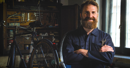 Bearded master master, specialist in bicycles, repairing a bicycle in his workshop, wheels, frame, wrench. Concept: pro bike, cycle passion, lifestyle.の写真素材