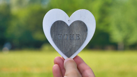 A silhouette of a woman holding a white heart in the form of a heart, the inscription "Home", a background of nature. Concept: a sweet house, a love to a family, hands in the shape of a heart, blue.の写真素材