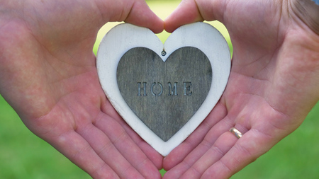 A silhouette of a woman holding a white heart in the form of a heart, the inscription "Home", a background of nature. Concept: a sweet house, a love to a family, hands in the shape of a heart, blue.の写真素材