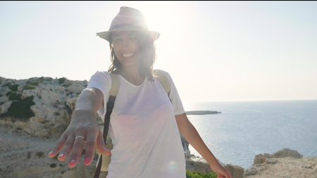 Portrait of a beautiful young girl (girl), holding a backpack, walking on the rocks, background with the sea (waves) & mountains. Concept: love, lifestyleの写真素材