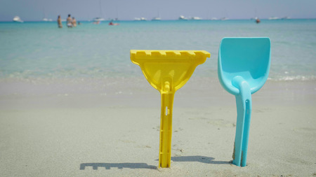 Children's forms yellow bucket, green shovel and pink watering can, different colors, background of sand and sea.の写真素材