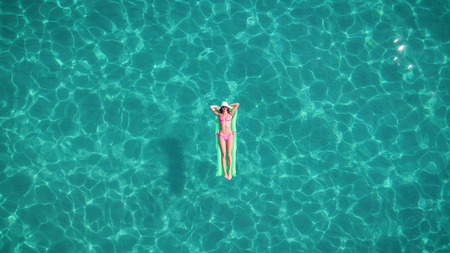 A beautiful young girl lies on a mattress in the open sea or pool, a pink bikini, hat, sunglasses, blue clear water, a top view. Concept: sea air, summer, travel, vacation, freedom, sun, enjoyの写真素材