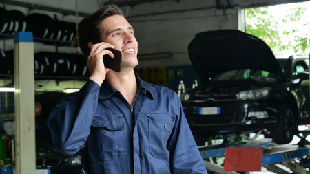 In a caretaker a mechanic uses the phone to respond to customer messages and calls as a car customer. Concept of: warranty, security, insurance and assistance, reviews, technology and customer care.の写真素材