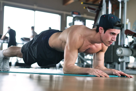 A boy, wearing a gym in a gym, trains his body to stay. Concept of: sport, gym, muscles and fitness