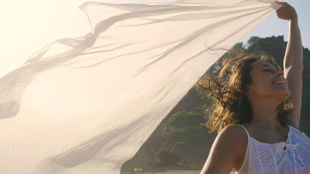 A beautiful young girl is walking along the seashore, wearing a white dress with a straw hat, white shawl, golden sand. Concept: sea rest, clean air, freedom, sun.の写真素材