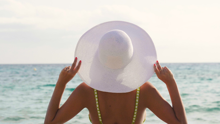 Portrait of a beautiful young girl, woman sunbathing on the sea, in a swimsuit, white hat, sea and sand background. Concept sea rest, clean air, freedom, sun, travel, waves, vacations, freedom, enjoyの写真素材