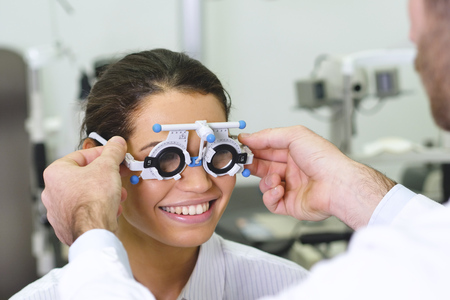 an ophthalmologist doing a visual examination for a customer at an optical center. Try the spectacles to the patient. Concept of: medical examination, assistance, optics and customer care.の写真素材