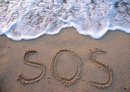 SOS - word drawn on the sand beach with the soft waveの写真素材