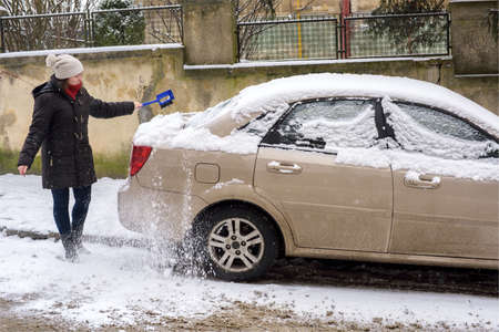 Woman cleans snow car outdoor during storm winter weather
