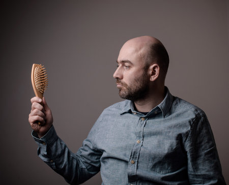 caucasian confused bald man trying hair brushの写真素材
