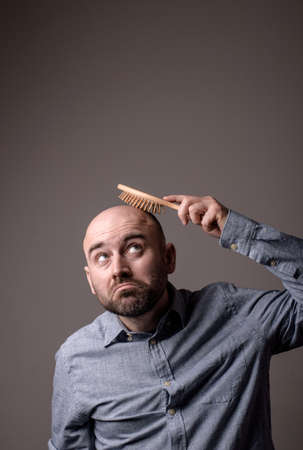 caucasian confused bald man trying hair brushの写真素材
