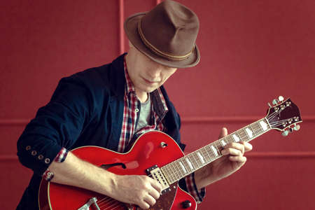 Musician in a hat with red electric guitarの写真素材