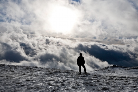 Silhouette of a man standing on top of a hill with dramatic clouds as backgroundの写真素材
