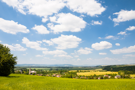 Village with church and tiled roof houses surrounded by cultivated fields and small woodsの写真素材
