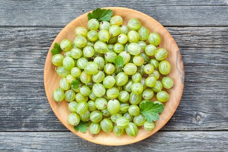 Juicy gooseberries with leaves in a wooden plate. Healthy eating backgroundの写真素材
