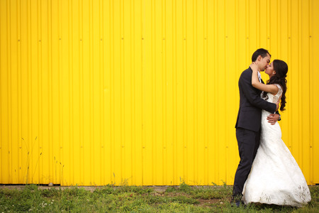 Bride and Groom kissing against yellow wallの写真素材