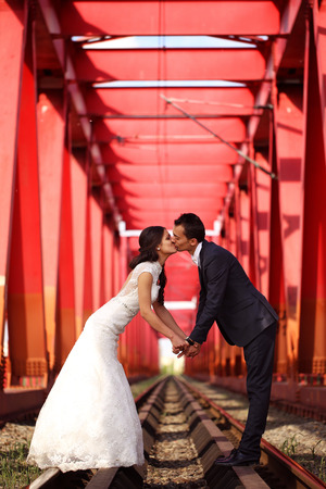 Bride and groom celebrating on a red bridgeの写真素材