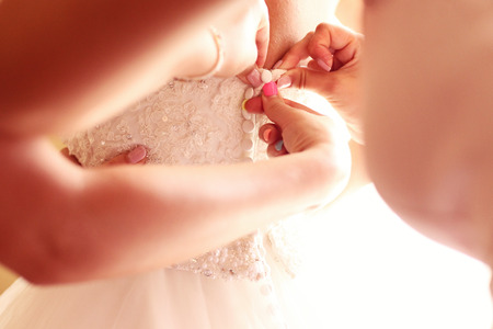 Hands of bridesmaid helpring the bride with wedding dressの写真素材