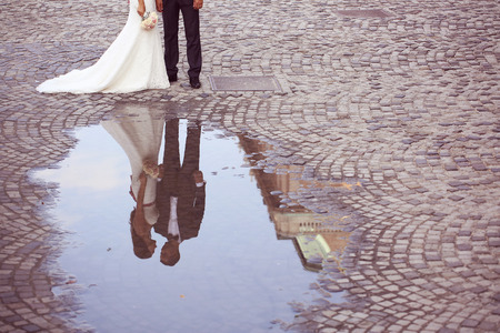 Bride and groom reflected in slop on paved roadの写真素材
